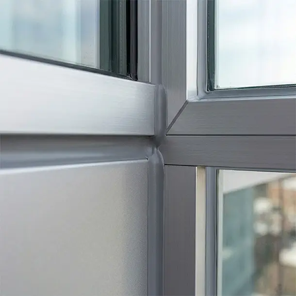 Close-up of gray window frame corner with clean, smooth sealant bead applied at joint, sealing glass and metal surfaces for weatherproofing.