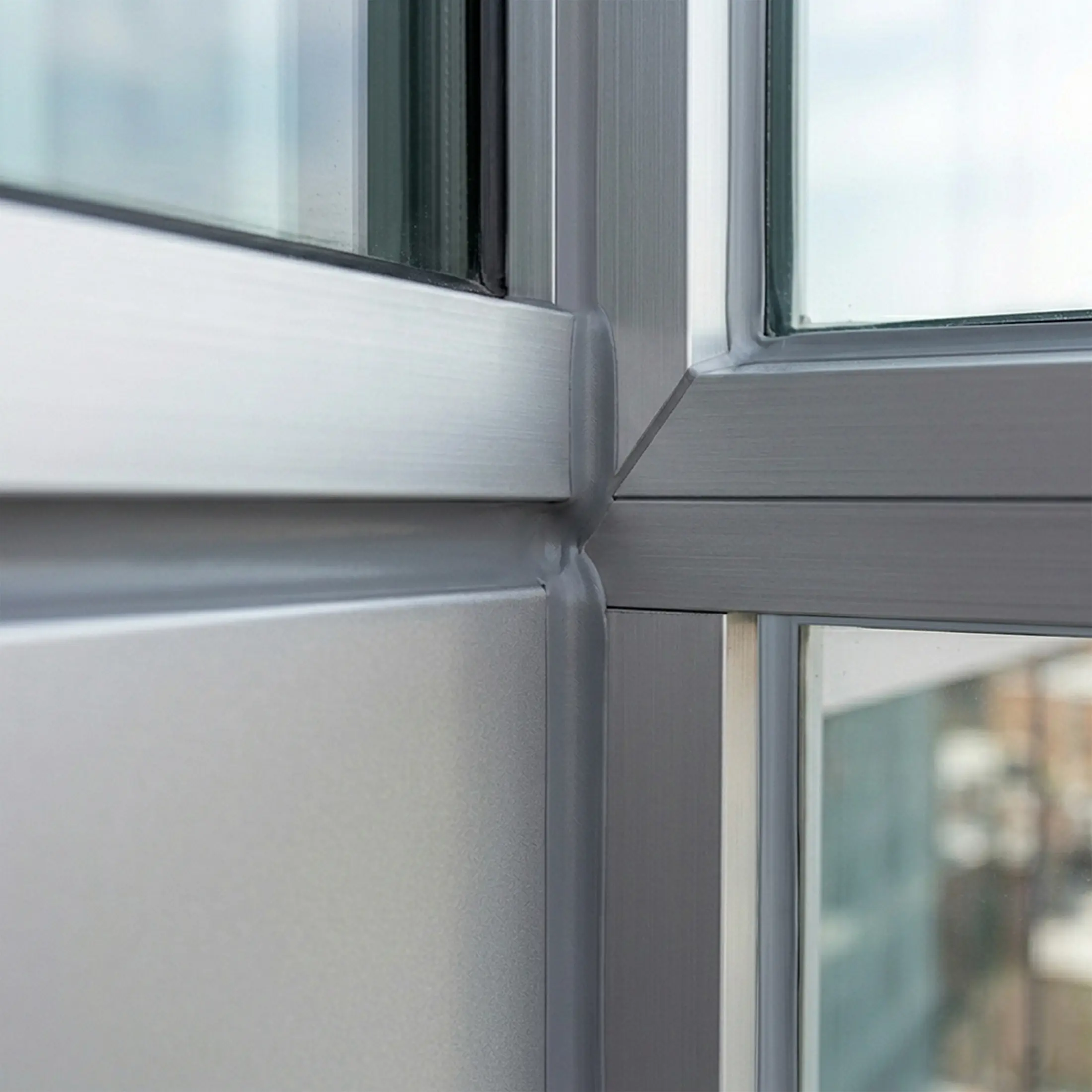 Close-up of gray window frame corner with clean, smooth sealant bead applied at joint, sealing glass and metal surfaces for weatherproofing.